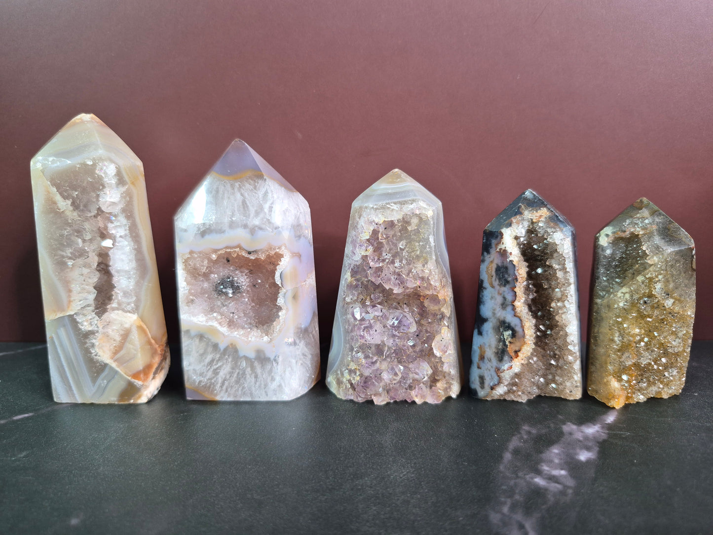 Five crystal towers with varying geode structures on a dark surface and brown background